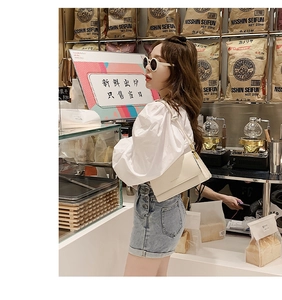 Detail of white minimalist crossbody bag with gold buckle shown in a stylish cafe setting