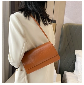 Detail of brown crocodile pattern shoulder bag with gold clasp on white blazer