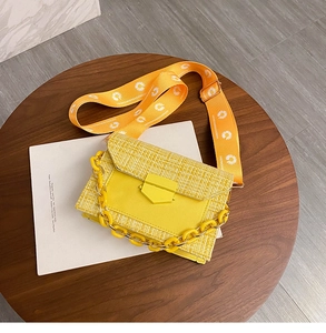 Detailed view of yellow crossbody bag with woven texture, chunky chain and daisy strap