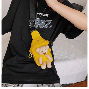 Detail of yellow canvas crossbody bag featuring a 3D teddy bear doll and black strap