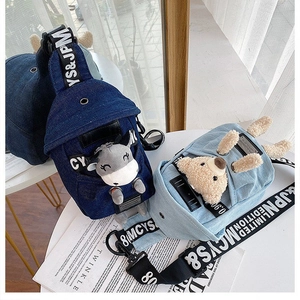 Detail of denim crossbody bags featuring plush bear and cow charms on a white table