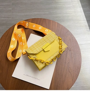 Detail of yellow woven crossbody bag featuring a daisy strap and thick plastic chain