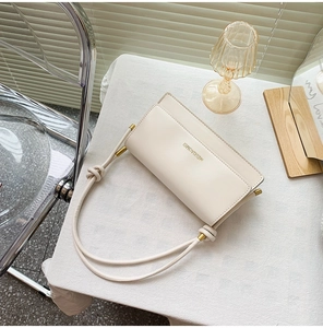 Detail of cream white leather crossbody bag with gold logo and knotted cord strap