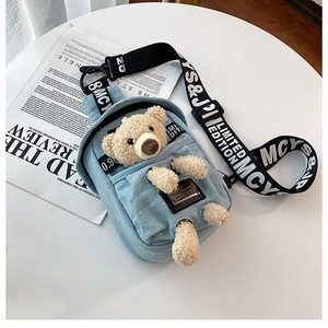Detail of denim chest bag featuring a cute plush bear decoration and wide woven strap