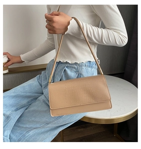 Detail of beige crocodile embossed baguette shoulder bag with gold metal accents