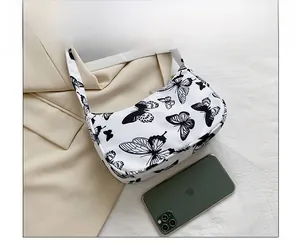 Detail view of white canvas underarm bag with black butterfly prints and a phone for size reference