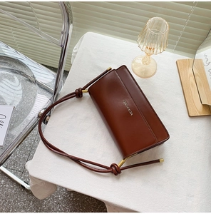 Close-up of a brown leather shoulder bag with gold logo and knot detail on a white table