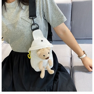 Close-up of white canvas chest bag featuring a plush brown bear doll and metal hardware