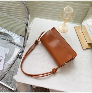 Close-up of brown leather handbag featuring unique knotted strap and gold hardware accents
