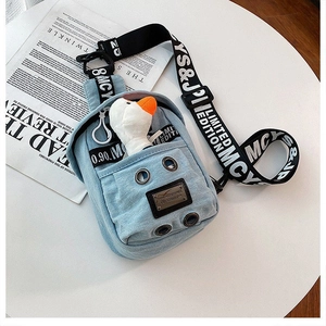 Detail of light blue denim crossbody bag with branded wide strap and plush goose toy