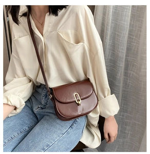 Detail einer dunkelbraunen Satteltasche aus Kunstleder mit goldener Schnalle am Outfit