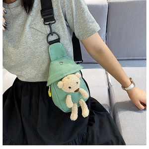 Close-up of light green canvas chest bag featuring a cute cream plush bear decoration