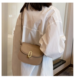 Detail der minimalistischen khakifarbenen Satteltasche mit Goldverschluss am Modell