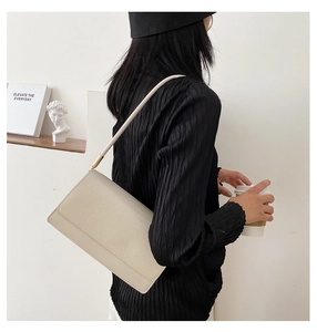 Detail of beige crocodile pattern underarm bag with gold accents on black shirt