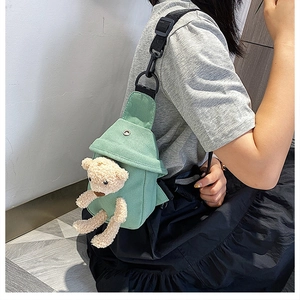 Close-up of sage green canvas crossbody bag featuring a cute beige 3D plush bear doll