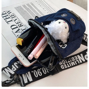Detail view of denim crossbody bag with metal eyelets and logo tag on a white desk
