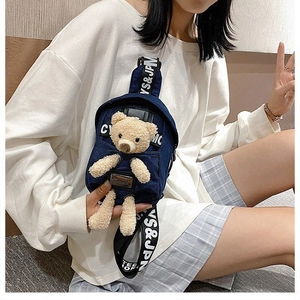 Detail of denim crossbody bag with cute plush bear and wide lettered strap on model