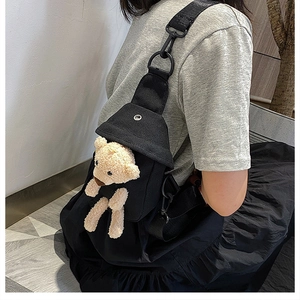 Detailed back view of a black canvas crossbody bag featuring a cute beige plush bear charm