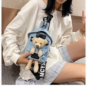 Detail of light blue denim crossbody bag featuring a 3D plush bear and lettered strap