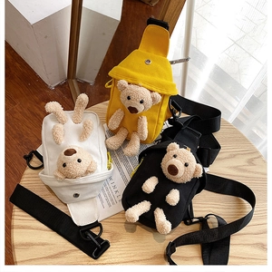 Three bear-themed canvas chest bags in yellow, white, and black on a wooden table