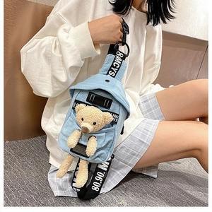 Detail of light blue denim crossbody bag with a cute plush bear in the front pocket