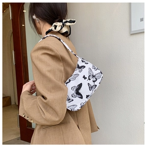 Detail of the butterfly pattern on a white canvas shoulder bag worn by a model