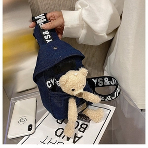Detail of dark blue denim chest bag featuring a plush teddy bear and printed logo strap
