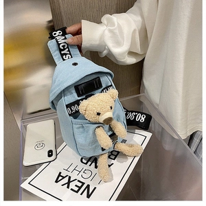 Detail of light blue denim chest bag featuring a cute plush bear inside the front pocket