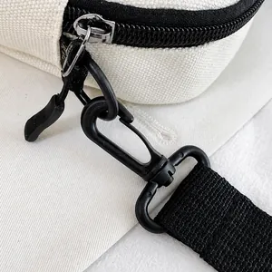 Detail shot of black metal lobster clasp and nylon strap on beige canvas crossbody bag