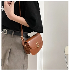 Braune Vintage-Satteltasche aus Leder mit goldener Schnalle an der Schulter des Models
