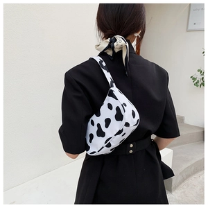 Detailed back view of a cow print underarm bag worn by a model against a white wall