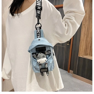 Detail of light blue denim chest bag featuring a cute plush bear decoration inside
