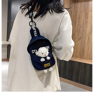 Detail of a denim crossbody chest bag featuring a white plush sheep doll and letter prints