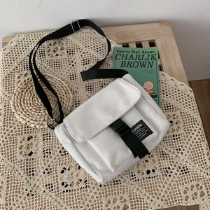 White canvas messenger bag with adjustable black strap and buckle in minimalist street style