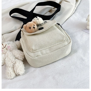 Detail of beige canvas crossbody bag with cute plush bear charms and black strap