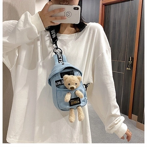 Detail of denim crossbody bag featuring a cute plush bear and branded nylon shoulder strap