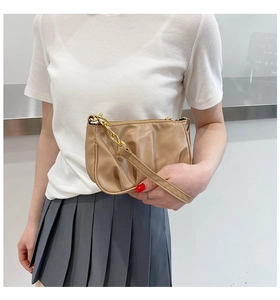 Fashionable beige pleated baguette bag with gold chain strap worn by a female model
