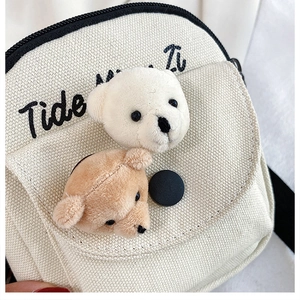 Detail shot of a beige canvas bag featuring 3D plush bear heads and black embroidery
