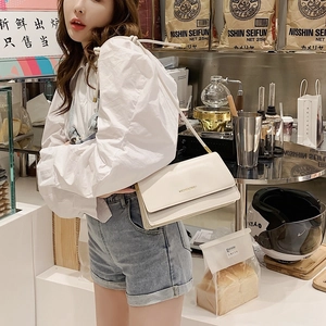 White minimalist chain crossbody square bag worn by a model in a cozy cafe setting