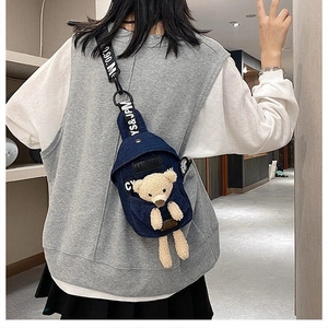 Detail of dark blue denim chest bag featuring a plush teddy bear and printed strap