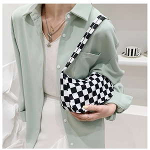 Close-up of black and white checkerboard baguette bag shown on shoulder with green shirt