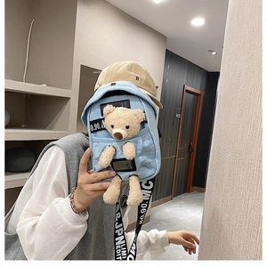 Detail of light blue denim crossbody bag featuring a 3D plush bear and wide graphic strap
