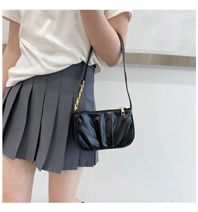 Detail of black pleated shoulder bag with gold chain strap and sleek zipper closure