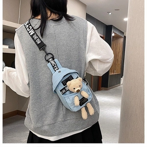 Detail of light blue denim chest bag featuring a cute teddy bear doll and branded strap
