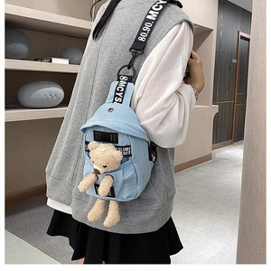 Detail of light blue denim chest bag with a cute beige plush bear and lettered strap