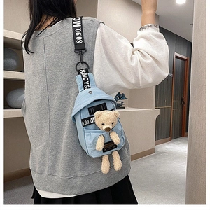 Detail of light blue denim chest bag featuring a cute 3D plush bear and lettered strap