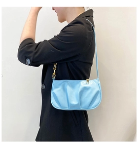 Detail of light blue pleated shoulder bag with gold chain strap on a black blazer