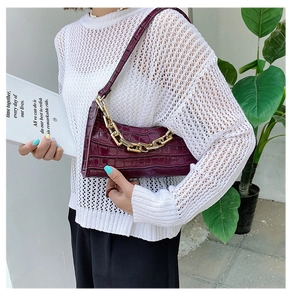 Detail of burgundy crocodile-embossed leather bag featuring a chunky gold chain strap