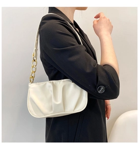 Detail of off-white pleated shoulder bag with chic gold chain strap on black blazer