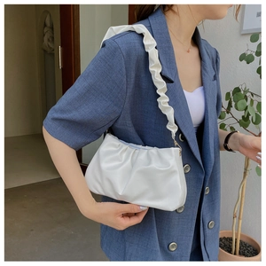 Close-up of a white pleated cloud bag with ruffled shoulder strap on a blue blazer